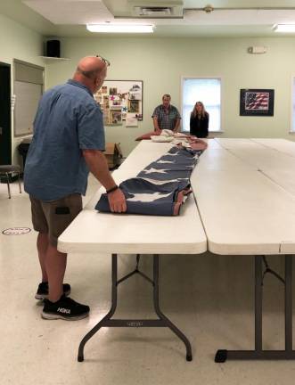 Bryan Ashley, Fred Rossi, the Repair Cafe’s knife and tool sharpener, and Abbey Ashley unfurled the flag on tables at the Warwick Senior Center.