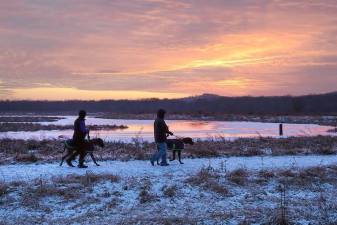 A winter solstice sunset silhouettes two hikers walking their dogs along Liberty Loop Trail at the Wallkill National Wildlife Refuge in Warwick on Dec. 21, 2019, the shortest day of the year.