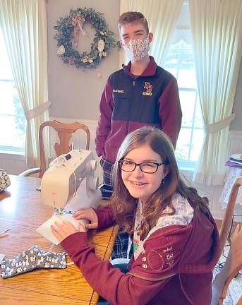 Grace McDonald, 14, sews masks modeled for the photograph by her brother PJ, 15.