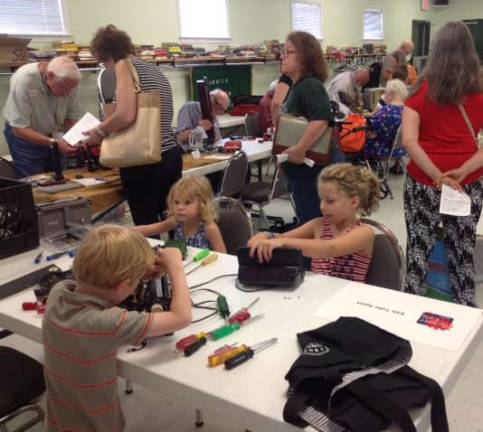 Adults line up for small electrics repairs while kids enjoy taking things apart.