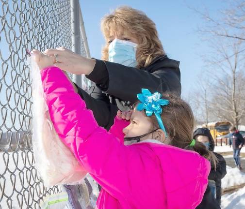 Kindergarten teacher Theresa Canfield helps Isabelle Piascik hang up a cold weather item on a fence at Pine Island Park.
