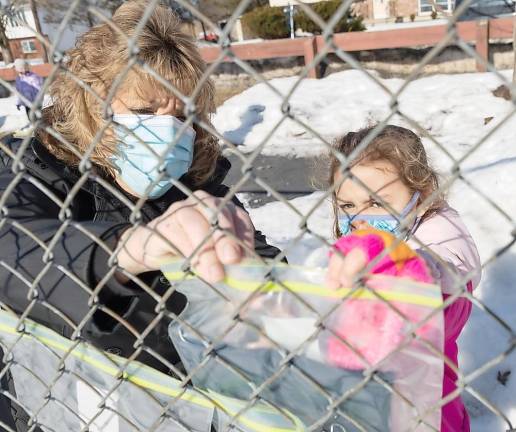 Kindergarten teacher Theresa Canfield helps Aubrey Rivera hang up a cold weather item donated by all of the classes at Pine Island Elementary School on a fence at Pine Island Park on Feb. 26.