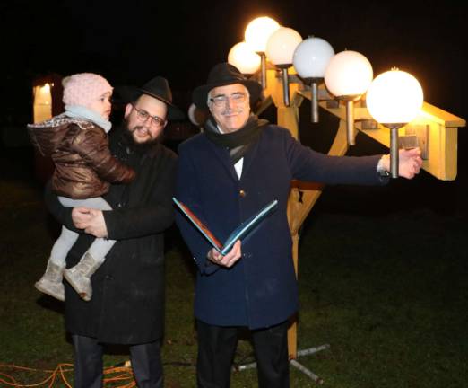 Photos by Roger GavanMorris Schwartzberg lights the first light as Rabbi Meir Borenstein and his daughter Raizel, 3, look on..