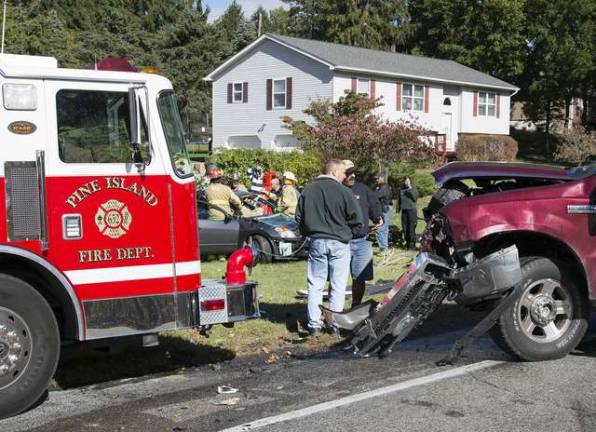 A Ford F350 pick up truck with heavy front-end damage sits at the intersection of County Route 1 and Little York Road in Warwick as Pine Island firefighters work to extricate the driver of the second car in the background.