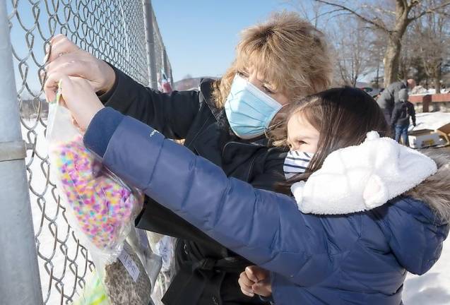 Kindergarten teacher Theresa Canfield helps Olivia Rodriguez hang up cold weather items on a fence at Pine Island Park.