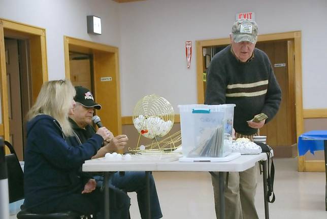 Calling bingo is Post Treasurer Sal Vargetto (seated), and helping him is Mary Francht, member of the Auxiliary. Standing is Post Service Officer Bernie White, handing prizes to the veterans.