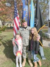 VFW Post 1708 Commander Ray Quattrini poses in front of the flag stand with his granddaughters, Samara and McKenna, who also led the crowd on hand in reciting the Pledge of Allegiance.
