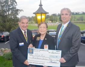Stan Martin, left, and Warwick Valley Rotary Club President Leo R. Kaytes present Carole Tjoa, Rotary District PolioPlus Chair, with a $4,000 donation to Rotary International’s effort to eliminate polio worldwide. In the background are some 250 Rotary Flags for Heroes displayed on the Chateau Hathorn lawn. Photo by Michael Tjoa.