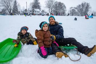 Jeff Church of Warwick smiles with his daughter Sophia Church, 5, and Lukas Church, 6, (left), all adorning blue hats and matching green sleds.