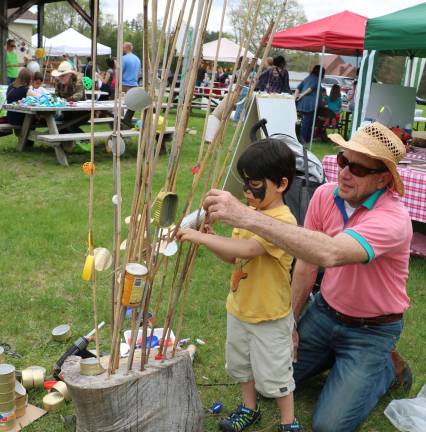 Photos by Roger Gavan Artist Roger Moss helps Benjamin Loibl, 4, decorate the artist's recycled cans tree, which he named &quot;Elmer Cantry.&quot;