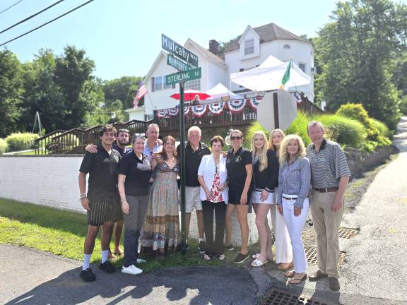 Mulcahy family. Denis Mulcahy (wearing black polo shirt) and his wife, Miriam (wearing white short sleeve jacket), immediately to the right of the street sign pole.