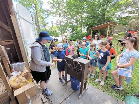 Warwick Historical Society docent Abigail Gurvich helps students use a corn sheller from the mid-1800s on their field trip last week.