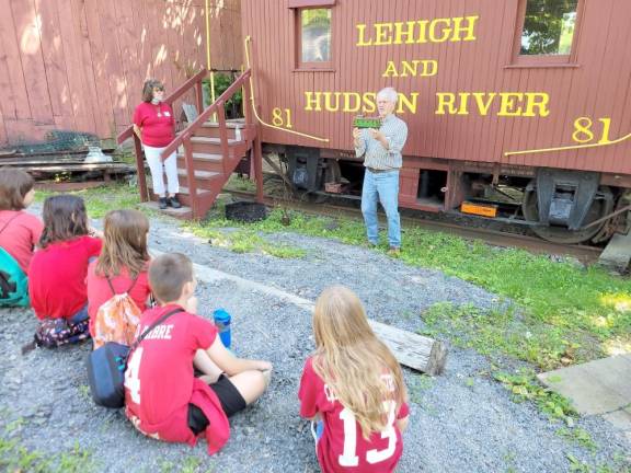 Annette Sanchez looks on as fellow Warwick Historical Society Education Committee member John Johansen gives a presentation to fourth graders about the Lehigh and Hudson River Caboose.