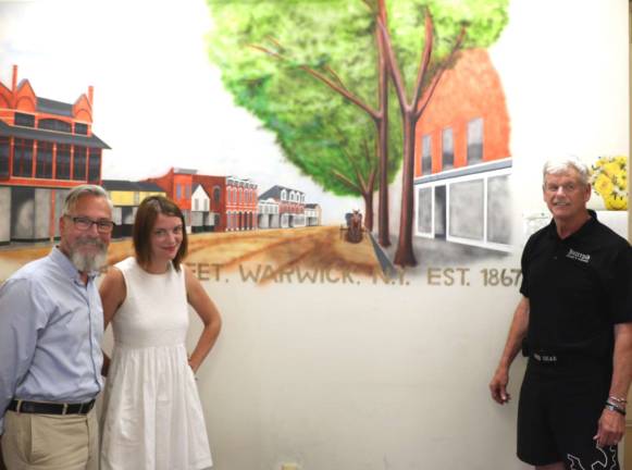 Photo by Roger Gavan Posing in front of a Village of Warwick Main Street mural by Rocco Mano are Mayor Michael Newhard, Sesquicentennial Project Manager Mary Collura and Village Trustee Bill Lindberg.