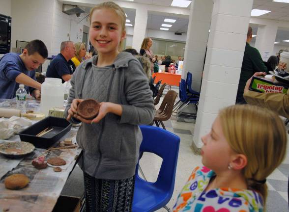 A young girl proudly shows the decorated clay pinch pot she created at Empty Bowls.