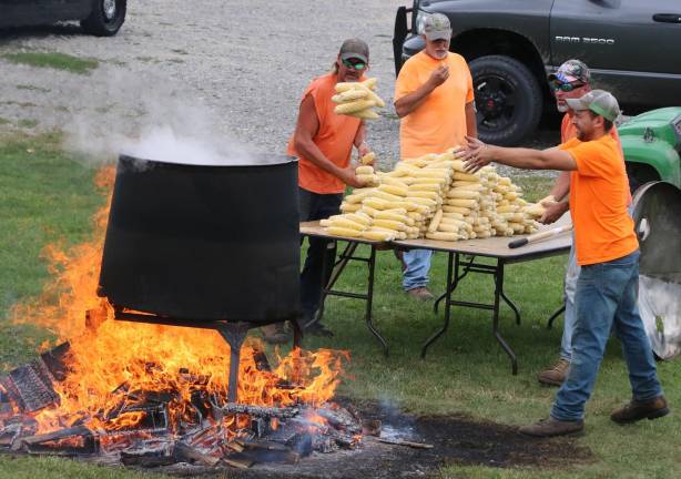 Members of the Town of Warwick DPW toss ears of corn into a huge kettle on an open fire.
