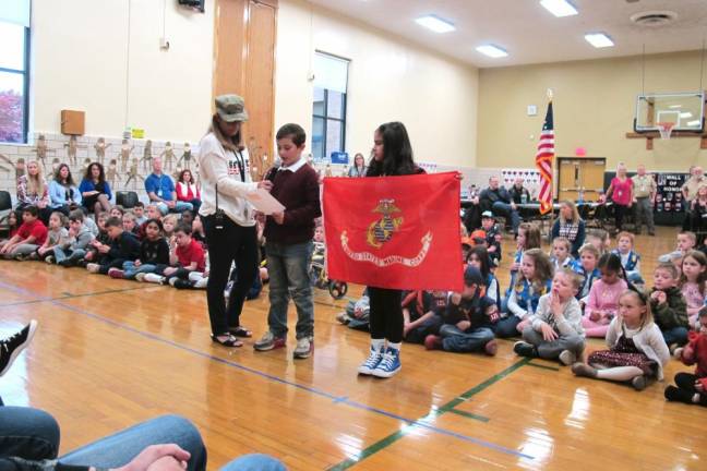 Principal Dianne Connolly stands with the third grade students giving a military flag branch presentation.