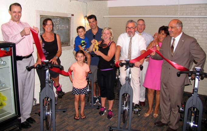 Photo by Roger Gavan On July 16, local officials and members of the Warwick Valley Chamber joined Jessica Hoye for the grand opening of Cycle Station. From left, Warwick Valley Chamber of Commerce President Paul Rafanello, instructor Diane Zimmerli, owner Jessica Hoye (cutting the ribbon) with her husband, Jeffrey, her son Preston, 4, and her daughter Abigayle, 6; Mayor Michael Newhard, Chamber Executive Director Michael Johndrow, Vice President Sherry Bukovcan, and Deputy Town of Warwick Supervisor James Gerstner.