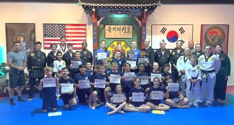 Warwick Junior Police Academy participants and overseeing officers show their self-defense training certificates at the Chosun Taekwondo Academy.