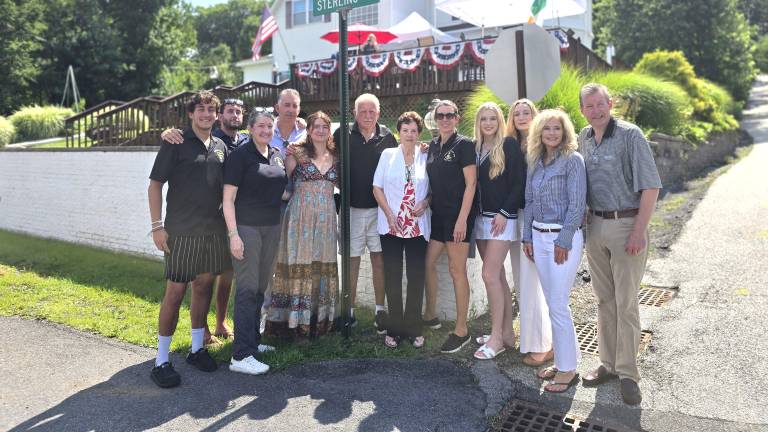 Mulcahy family. Denis Mulcahy (wearing black polo shirt) and his wife, Miriam (wearing white short sleeve jacket), immediately to the right of the street sign pole.